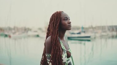 Afrika örgülü güzel bir kadın limanda iskele boyunca yürüyor ve deniz manzarasına bakıyor.