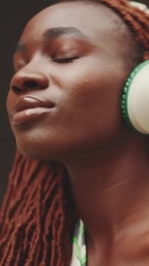 Kulaklıklı, Afrika örgülü, sokakta müzik dinlemekten keyif alan güzel bir kadının yakın çekimi. Şık kız gözleri kapalı müzik dinliyor.