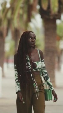 Afrika örgüleri takan muhteşem bir kadın caddede yürür durur. Şık kız başını çevirir ve kameraya bakar.