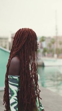 Üzerinde Afrika örgüsü olan muhteşem kadının profili limandaki limanda duran yat ve gemilere bakıyor.