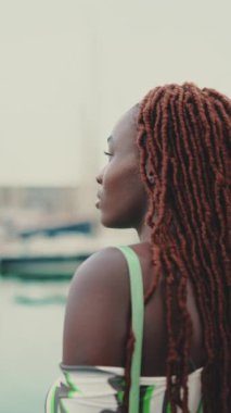 Üstü örülü Afrikalı kadın limandaki rıhtımda duran yat ve gemilere bakıyor. Arka plan
