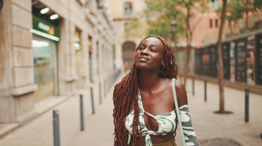 Afrika örgülü güzel bir kadın caddede yürüyor. Havalı gülümseyen kız binaların üst katlarına bakıyor.