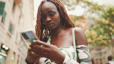 Üstü başı Afrika örgülü muhteşem bir kadın sokakta dikiliyor ve cep telefonu kullanıyor. Şık kız akıllı telefondan mesaj yazıyor.