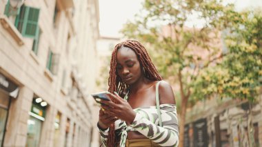 Üstü başı Afrika örgülü muhteşem bir kadın sokakta dikiliyor ve cep telefonu kullanıyor. Şık kız akıllı telefondan mesaj yazıyor.