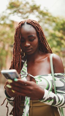 Üstü başı Afrika örgülü muhteşem bir kadın sokakta dikiliyor ve cep telefonu kullanıyor. Şık kız akıllı telefondan mesaj yazıyor.