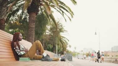 Profile göre, Afrika örgülü muhteşem bir kadın üst tarafta oturuyor ve pantolonu da bankta dinleniyor.