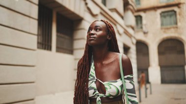 Afrika örgülü güzel bir kadın caddede yürüyor. Havalı gülümseyen kız binaların üst katlarına bakıyor.