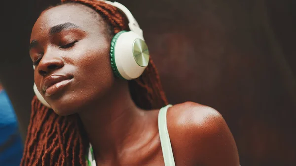在外面的街上 戴着非洲辫子 头戴耳机欣赏音乐的美女的特写 一个时髦的女孩闭着眼睛听音乐 — 图库照片