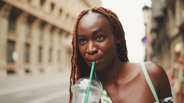 Clouse-up, gorgeous woman with African braids wearing top stands on the sidewalk next to the road waiting for taxi