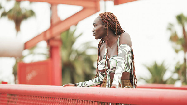 Gorgeous woman with African braids wearing top stands on the bridge