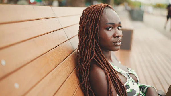 Profile göre, Afrika örgülü muhteşem bir kadın üst tarafta oturuyor ve pantolonu da bankta dinleniyor.