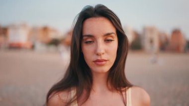 Close-up Beautiful brown-haired woman with long hair sits on the beach. Gorgeous girl with freckles and long eyelashes looks at the camera. slow motion