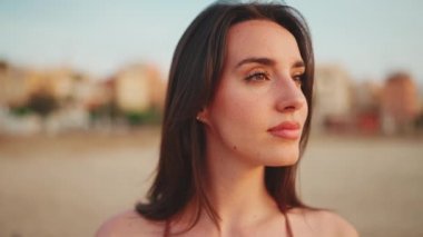 Uzun saçlı, güzel, kahverengi saçlı kadın kumsalda ayakta duruyor. Uzun kirpikleri ve çilleri olan güzel bir kız. Yavaş çekim