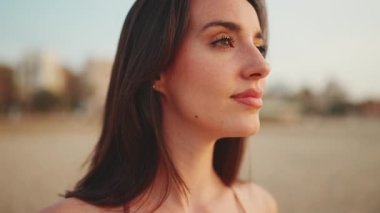 Uzun saçlı, güzel, kahverengi saçlı kadın kumsalda ayakta duruyor. Uzun kirpikleri ve çilleri olan güzel bir kız. Yavaş çekim