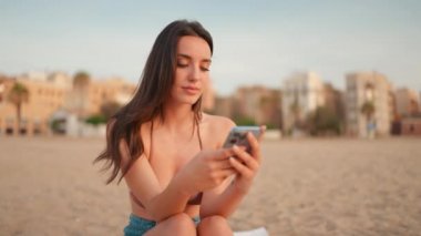 İnce, kahverengi saçlı, uzun saçlı bir kadın kumsalda cep telefonu kullanıyor. Çok güzel bir kız akıllı telefona bilgi aktarıyor. Kamera sağa doğru yana hareket ediyor.