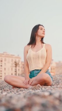 Kumsalda oturan, uzun saçlı, güzel, kahverengi saçlı bir kadın var. Üstü başı ve kot şortu olan güzel bir kız. yavaş çekim