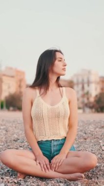 Kumsalda oturan, uzun saçlı, güzel, kahverengi saçlı bir kadın var. Üstü başı ve kot şortu olan güzel bir kız. yavaş çekim