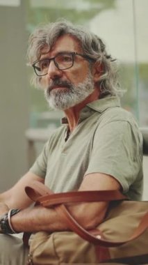 Gri saçlı, sakallı, sıradan kıyafetler giyen orta yaşlı bir adam toplu taşıma durağında oturuyor. Gözlüklü ve çantalı olgun bir adam tramvay istasyonunda bekliyor.