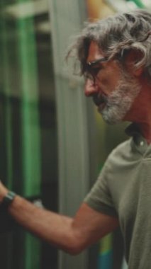 Gri saçlı ve sakallı orta yaşlı bir adamın profili toplu taşıma durağında tramvaya biniyor. Omzunda çanta olan gözlüklü bir beyefendi tramvaya biniyor.