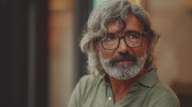 Gri saçlı, sakallı, sıradan kıyafetler giyen düşünceli, orta yaşlı bir adam sokak kafesinde oturuyor. Gözlüklü olgun beyefendi aromalı kahve içer.