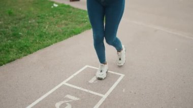 Close-up of young woman hopscotching on city playground. Closeup of the legs of girl jumping on the drawn cells on the pavement