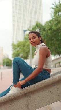 Uzun kahverengi saçlı, beyaz bluz giyen, oturan ve kameraya bakan hoş, bronz tenli bir kadın.