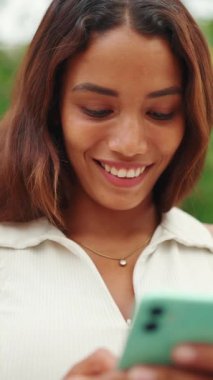 Clouse-up, uzun siyah saçlı, beyaz bluzlu güzel kız bankta oturuyor ve cep telefonu kullanıyor. Sosyal ağlarda cep telefonuyla yazan gülümseyen genç bir kadın.