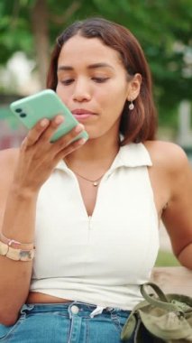 Uzun siyah saçlı, beyaz bluzlu güzel bir kız bankta oturuyor ve cep telefonu kullanıyor. Genç kadın sesli mesaj gönderiyor.