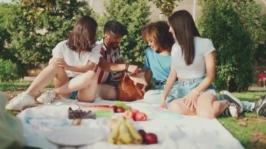 Happy smiling young multinational people at picnic on summer day outdoors. Four friends have fun weekend together, relaxing in the park at picnic