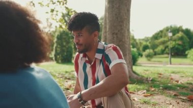 Happy smiling young multinational people at picnic on summer day outdoors. Four friends talking while spending the weekend together, relaxing in the park at picnic