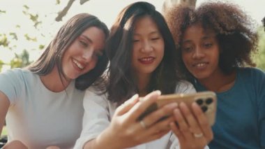 Mutlu, çoklu etnik çeşitlilikte gülümseyen gençler yaz günü açık havada piknik yapıyorlar. Arkadaş grubu cep telefonu kullanır, video izler, sosyal ağlar
