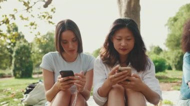 Young multi ethnic women browsing videos, photos, social networks on the phone at picnic on summer day outdoors