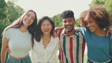 Mutlu çok ırklı gençler, yaz günü açık havada piknikte kameraya poz vermekten hoşlanırlar. Bir grup arkadaş kameraya bakar ve neşeyle güler.