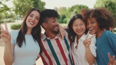 Happy, lovely multiethnic young people posing for the camera on summer day outdoors. group of friends hugging each other smiling at the camera while standing on path in the park