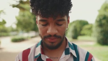 Kıvırcık saçlı, çizgili gömlek giyen, kameraya bakıp gülümseyen genç adamın yakın çekimi.