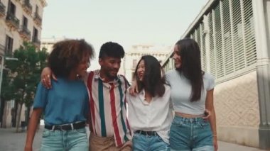 Mutlu çoklu etnik çeşitlilikte genç insanlar yaz günü açık havada kucaklaşarak yürürler. Bir grup arkadaş sokakta yürürken neşeyle konuşuyor ve gülüyorlar.