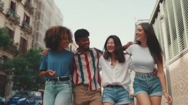 Mutlu çoklu etnik çeşitlilikte genç insanlar yaz günü açık havada kucaklaşarak yürürler. Bir grup arkadaş sokakta yürürken neşeyle konuşuyor ve gülüyorlar.