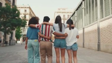 Mutlu çoklu etnik çeşitlilikte genç insanlar yaz günü açık havada kucaklaşarak yürürler. Bir grup arkadaş sokakta yürürken neşeyle konuşuyor ve gülüyorlar. Arka plan