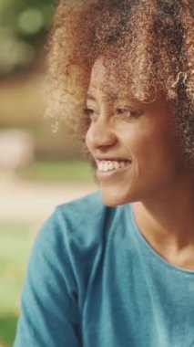 Kıvırcık saçlı, mavi tişörtlü, parkta piknik yapan, arkadaşlarıyla sohbet eden genç bir kadının yakın çekimi.