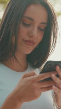 Clouse-up, uzun kahverengi saçlı, beyaz ekin bluzlu güzel bir kadın yaz günü parkta piknik yapıyor, arkadaşlarıyla konuşuyor, cep telefonu kullanıyor.