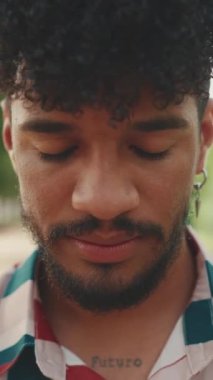 Kıvırcık saçlı, çizgili tişörtlü ve kameraya bakıp gülümseyen genç adamın yakın çekimi.