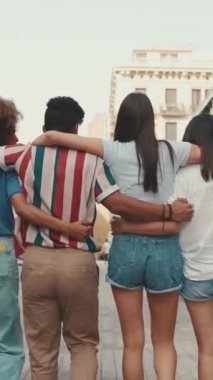 Mutlu çoklu etnik çeşitlilikteki gençler yaz günü açık havada kucaklaşarak yürürler. Bir grup arkadaş sokakta yürürken neşeyle konuşuyor ve gülüyorlar. Arka plan