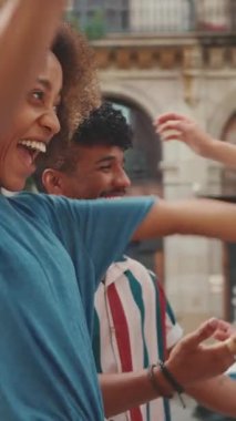 VERTICAL VIDEO: Young multiethnic couple walk laughing down the street on warm summer day, meeting friends, enjoy meeting and hugging