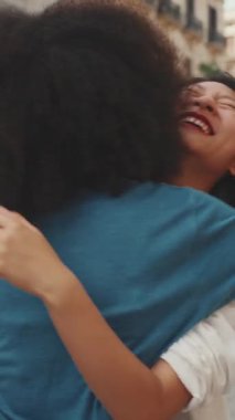 VERTICAL VIDEO: Young multiethnic women walk laughing down the street on warm summer day, meeting couple friends, enjoy meeting and hugging