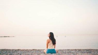 Kumsalda deniz manzaralı, uzun saçlı güzel bir kadın oturuyor. Üstü başı ve kot şortu olan güzel bir kız.. 