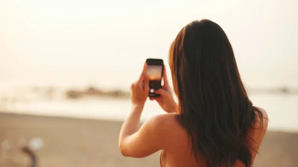 Piękna Brązowłosa Kobieta Długimi Włosami Używa Telefonu Komórkowego Stojąc Plaży — Zdjęcie stockowe