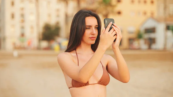 Piękna Brązowłosa Kobieta Długimi Włosami Używa Telefonu Komórkowego Stojąc Plaży — Zdjęcie stockowe