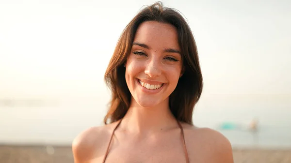Close-up of beautiful brown-haired woman with long hair and freckles smiling and looking at the camera.