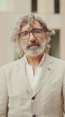 Gözlüklü, sakallı, gri ceketli, olgun bir iş adamı kollarını kavuşturup kameraya bakıyor. Ofisin dışında dikilirken orta yaşlı yönetici kameraya poz veriyor.