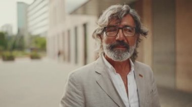 Gözlüklü, gri ceketli, sakallı, olgun bir işadamı gibi modern binaların önünden geçeceğiz.